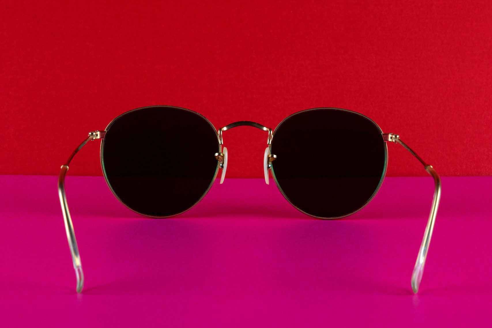 Round sunglasses on pink and red background.