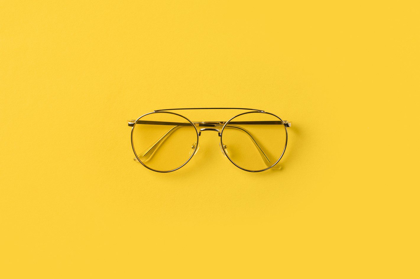 Gold-rimmed glasses on yellow surface
